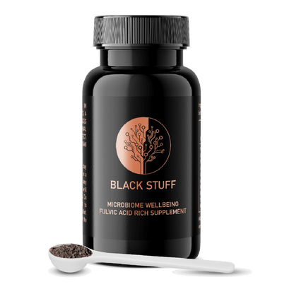 A black bottle labeled 'BLACK STUFF' with a gold tree logo, alongside a white dosing scoop filled with black powder.