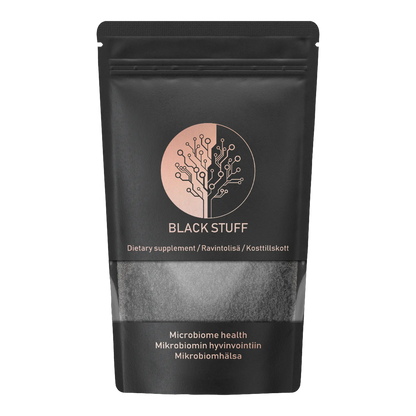 A black resealable pouch labeled "BLACK STUFF" with a circular logo resembling a tree made of circuit lines. The packaging states "Dietary supplement" in multiple languages and "Microbiome health" in English, Finnish, and Swedish. The lower part of the pouch has a transparent window showing black powder inside.